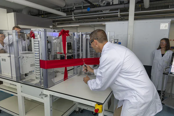 Mensch und Maschine eröffnen gemeinsam - Jon Novak beim Ribbon Cut – synchron mit dem Roboterarm des neuen Automatisierungssystems.