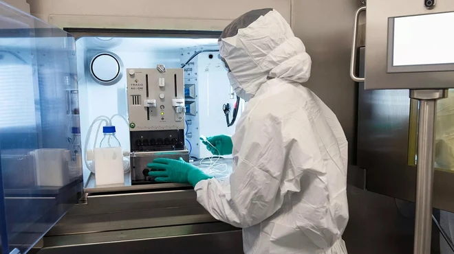 Un collaborateur portant un équipement de protection individuelle complet et utilisant des équipements spécialisés sur la ligne de production de thérapie par radioligands.