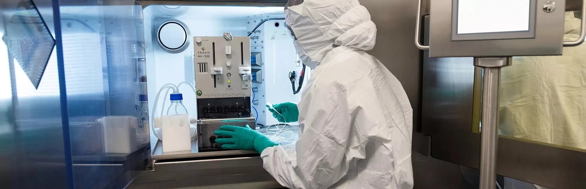 Un collaborateur portant un équipement de protection individuelle complet et utilisant des équipements spécialisés sur la ligne de production de thérapie par radioligands.