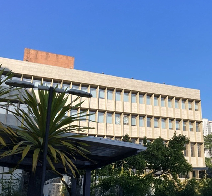 Foto do prédio da Novartis São Paulo. O prédio é bege, com janelas azuladas e possuí árvores ao redor. O céu está azul e é manhã. 