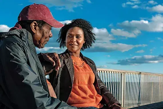 Homem e mulher afrodescendente em, encostados em uma grade em um dia de sol com nuvens no céu