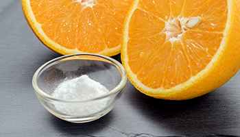 Une orange coupée et une coupelle contenant de la vitamine C en poudre