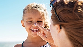 Une femme applique de la crème solaire sur le visage d'une enfant