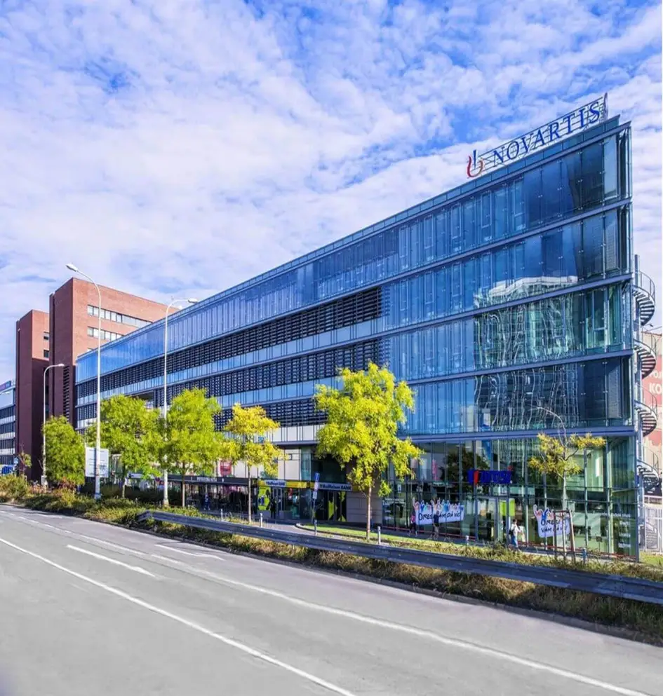 Moderní prosklená administrativní budova společnosti Novartis v Praze za slunného dne