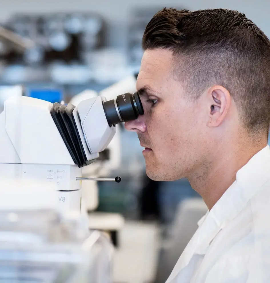 Profile close-up of a healthcare professional looking through a high-tech microscope in a lab