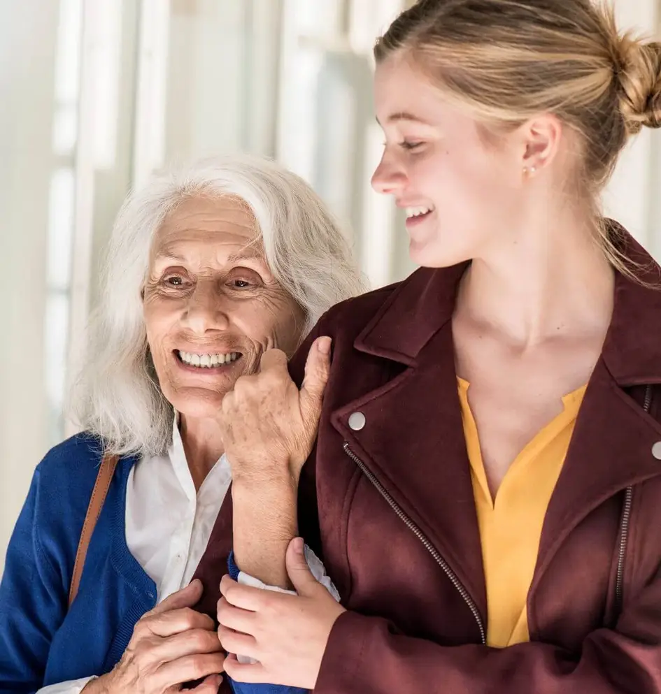 A smiling young woman supportive-holding the arm of a happy senior woman while walking together