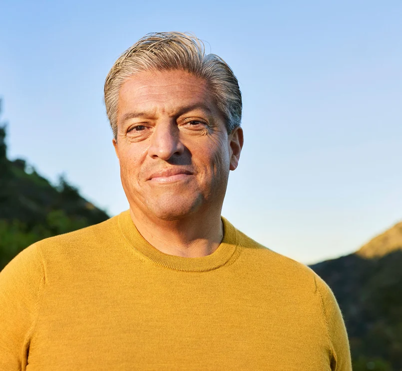 Ältere Person in gelbem Pullover draußen bei Sonnenuntergang.