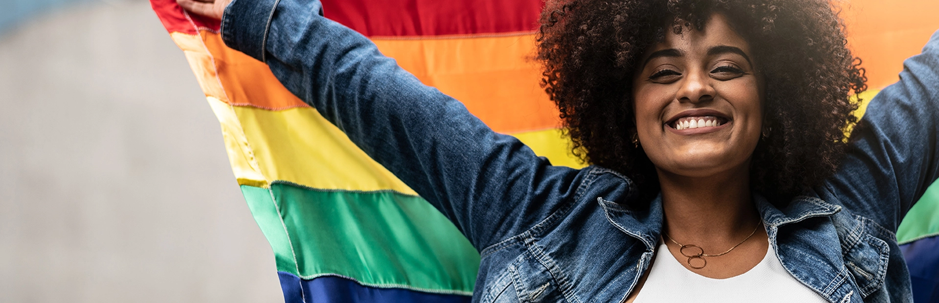 Eine lächelnde Frau hält eine Regenbogenflagge hoch