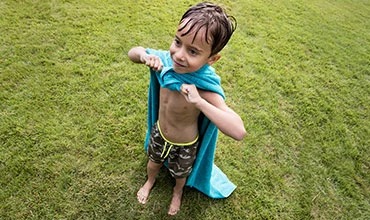 Kind spielt draußen mit einem Handtuch auf dem Gras.