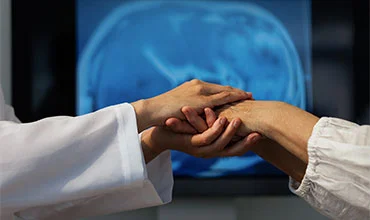 Ärzte untersuchen die Hand eines Patienten, im Hintergrund ein Gehirnscan.