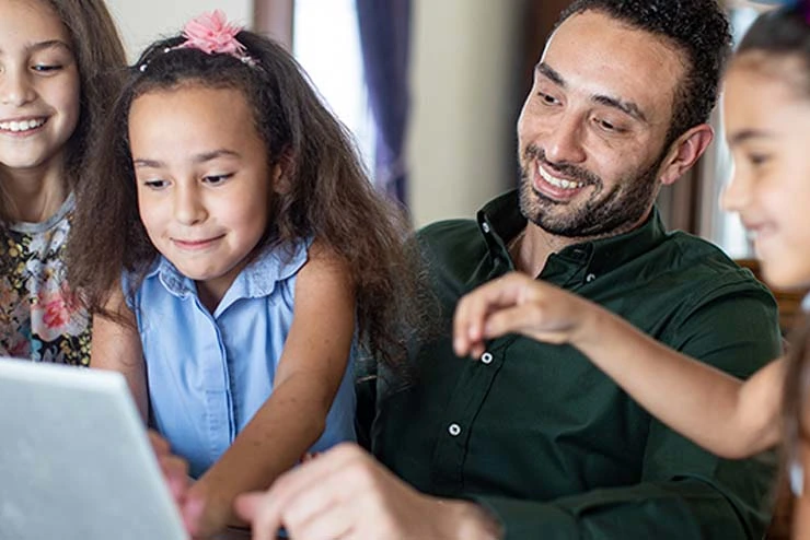 Ein Vater sitzt mit seinen Kindern am Laptop und zeigt ihnen etwas