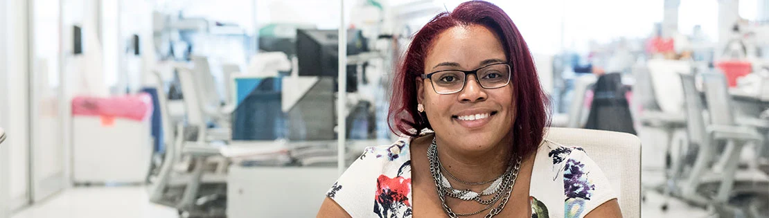 Wissenschaftlerin sitzt im Labor und lächelt in die Kamera