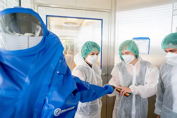 Standortleiterin zeigt Schutzanzug