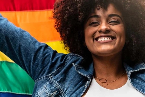Eine lächelnde Frau hält eine Regenbogenflagge hoch