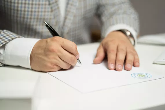 Person im Jacket schreibt auf einem Blatt Papier