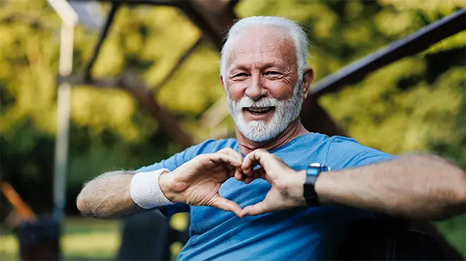 Älterer Mann auf Parkbank formt Herzhände