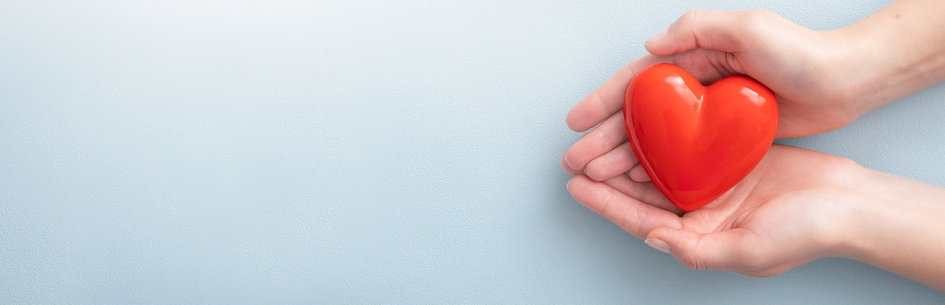 Manos sujetando un corazón rojo de plástico en fondo azul 