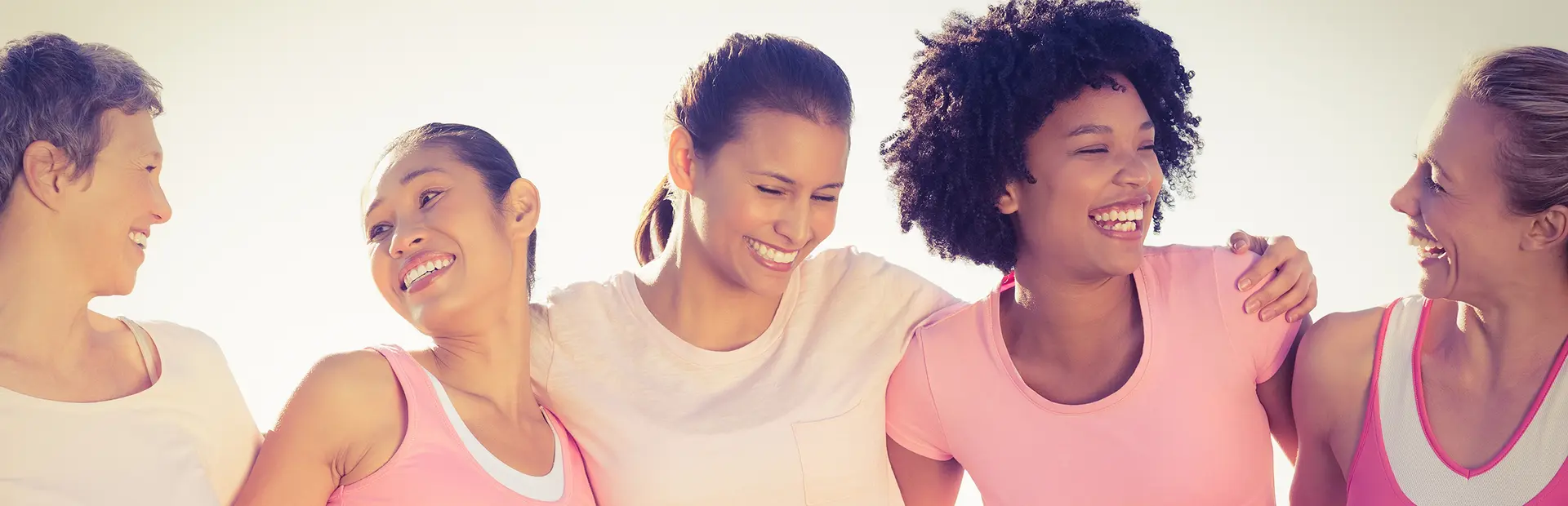 Cinco mujeres en fila abrazándose por los hombros y sonriendo 