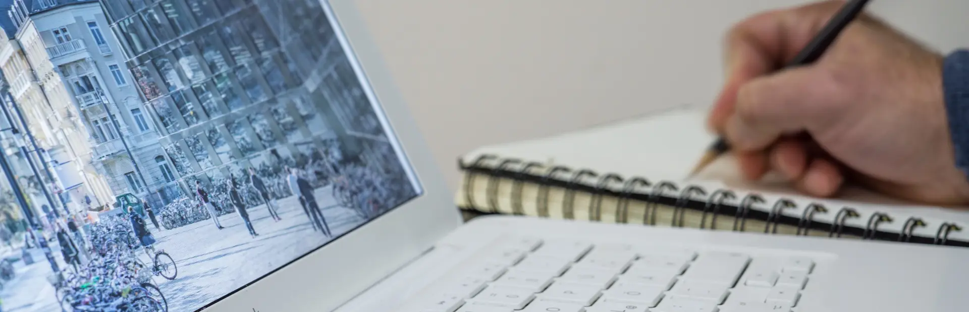 persona escribiendo con un lápiz en un cuaderno frente a la pantalla de su ordenador