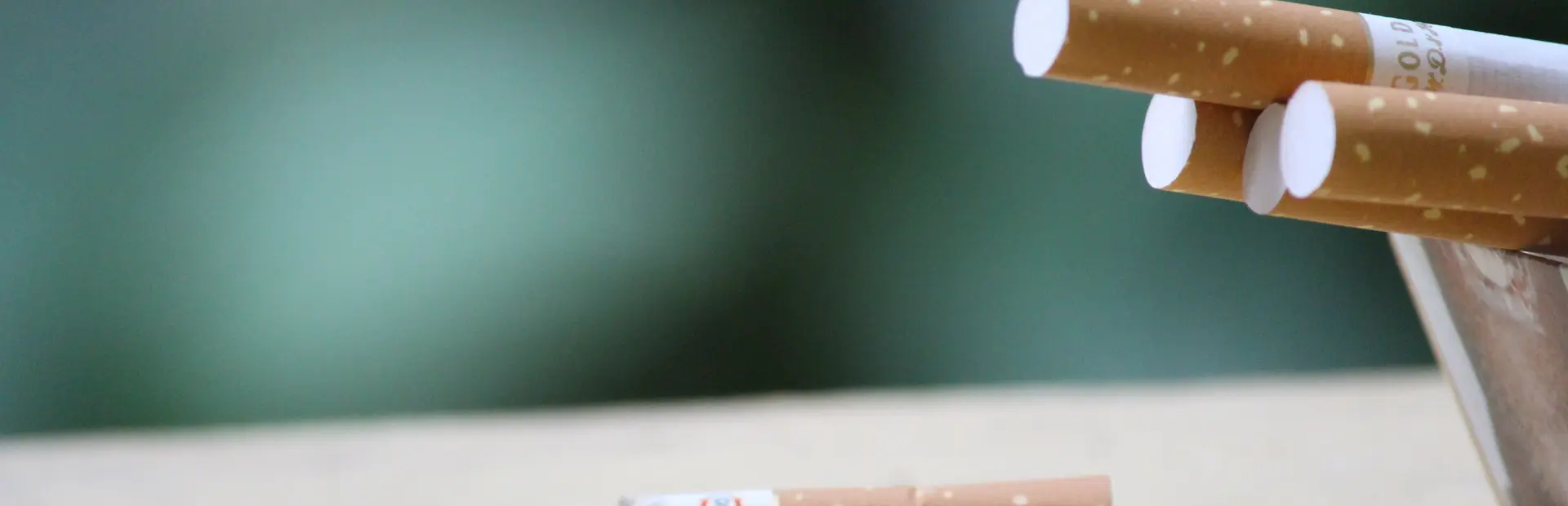 Cigarrillos en cenicero, uno de ellos apagado en la superficie de la mesa rodeado de cenizas