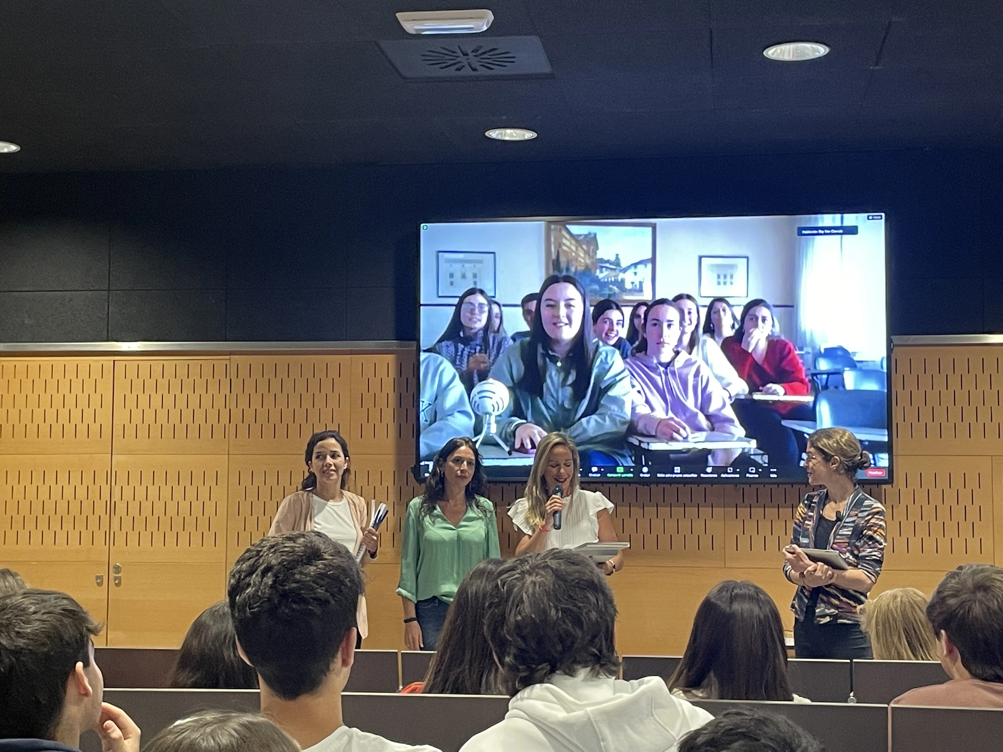 El jurado anunciando el premio y varios miembros del eguipo ganador detrás, en pantalla, conectados vía streaming desde Antequera. Las miembros del jurado son, de izquierda a derecha, Gabriela Garcia, del parque Científico y Tecnológico Cartuja; Charo Cobano, de Fundación Pública Andaluza Progreso y Salud; y Ana Escacena, de Novartis.