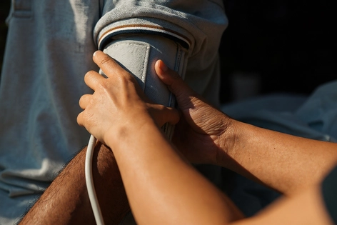 Person checks blood pressure of another person in a clinical setting