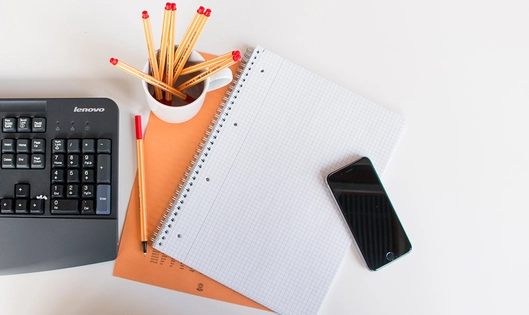 A notebook, a keyboard, a phone and pens