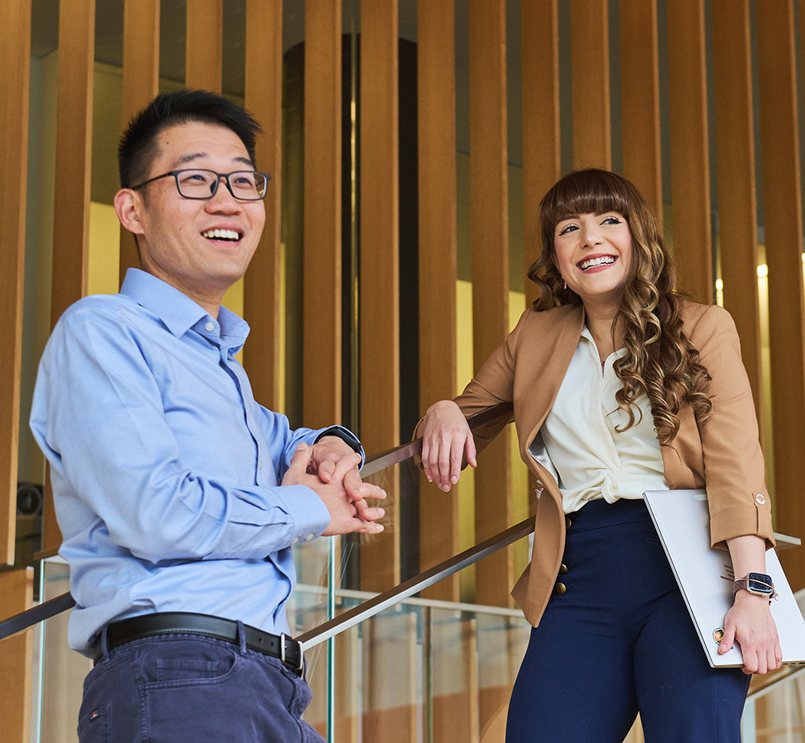 Two business people smiling and standing against a wall