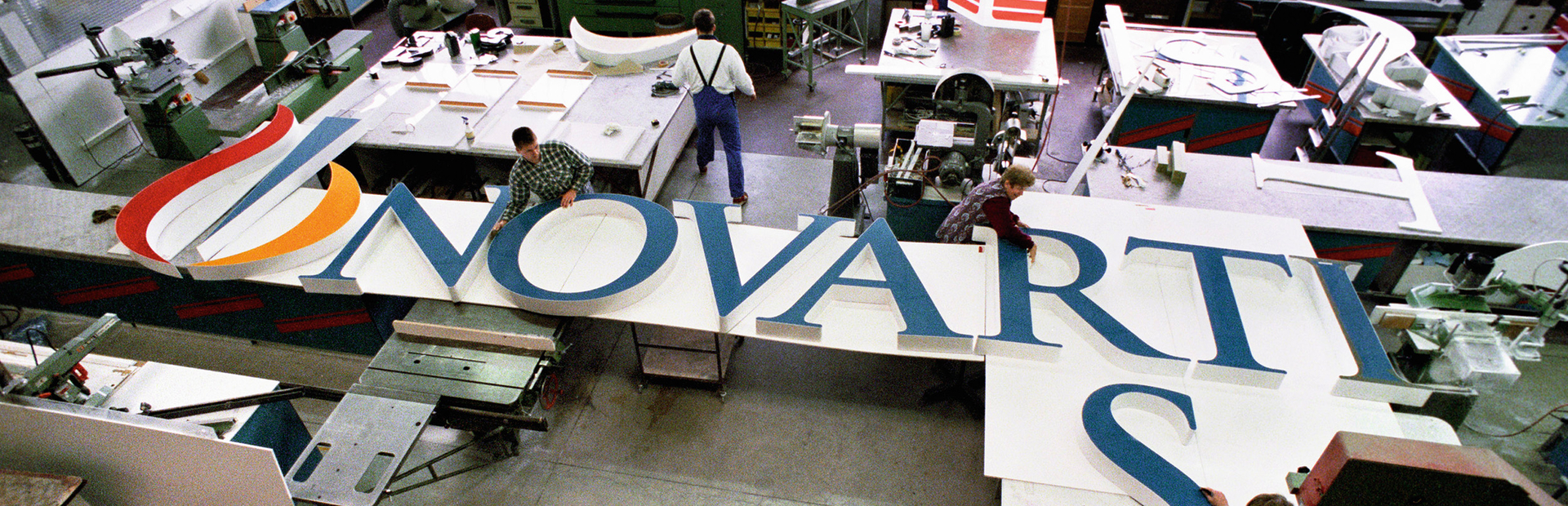 Several people working at assembling the big letters forming "Novartis" that will be installed at the top of a building on the Novartis Basel campus