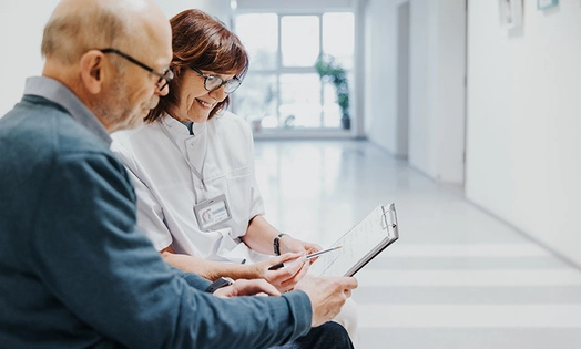 A doctor and patient sitting in a hospital, reading a document together.