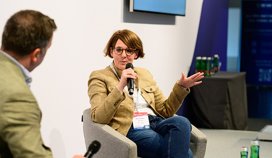 woman on stage talking and holding a microphone