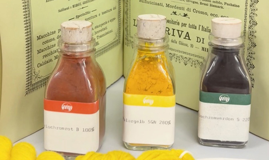 Three small corked bottles with red, yellow, and dark dyes, displayed in front of printed sheets.
