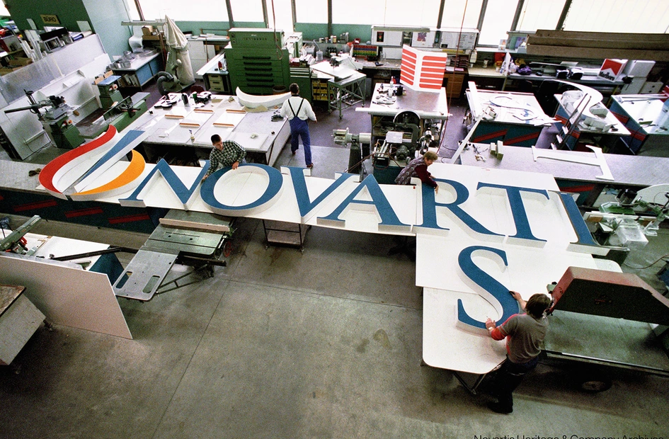 Several people working at assembling the big letters forming "Novartis" that will be installed at the top of a building on the Novartis Basel campus