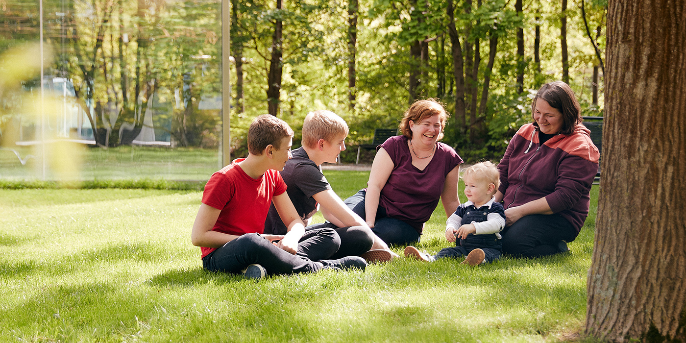 A family laugh together in the shade of a tree on a sunny day