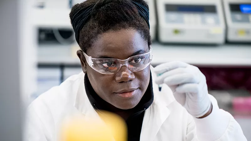 A researcher at Novartis wearing safety glasses is looking at test tube.