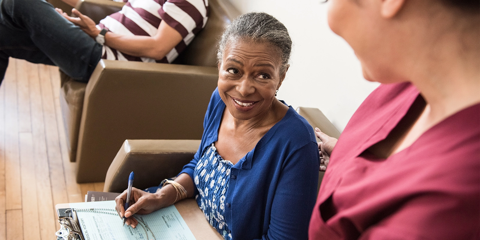 Female patient smiles at female HCP in waiting room of doctor’s office