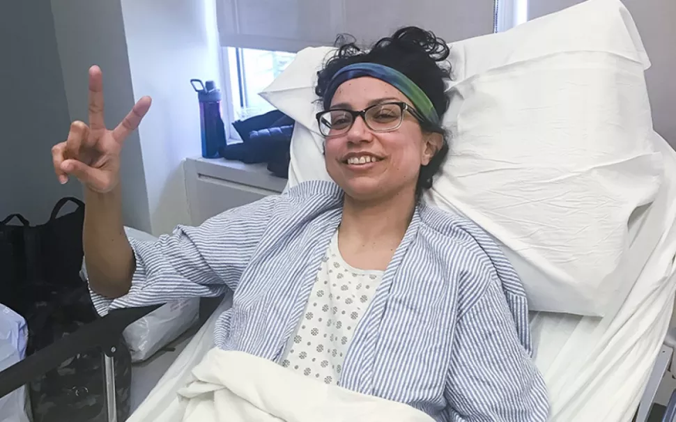 A kidney patient is lying in a hospital bed, smiling and making a victory sign