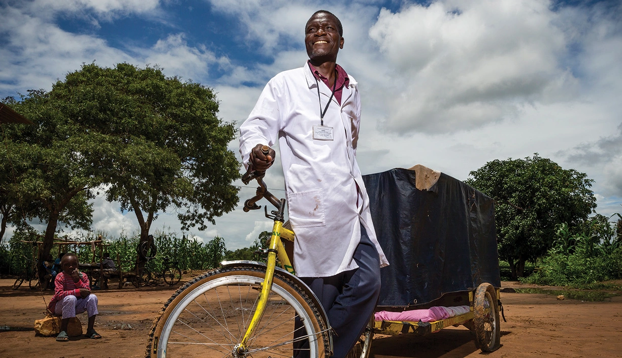 HCP wearing a medical coat pulling a cart bicycle in rural african village