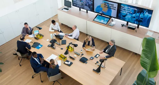 Overhead view of a meeting room with people in the foreground and screens in the background