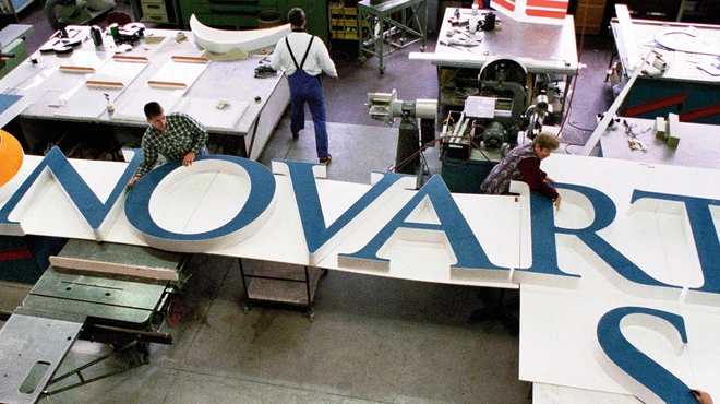 Several people working at assembling the big letters forming "Novartis" that will be installed at the top of a building on the Novartis Basel campus