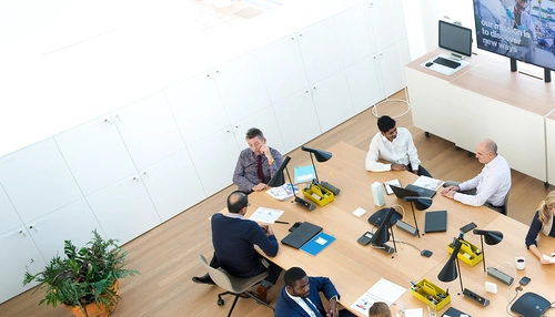 Overhead view of a meeting room with people in the foreground and screens in the background