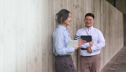 Two business people smiling and standing against a wall