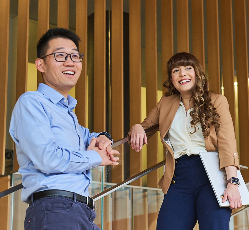 Two business people smiling and standing against a wall