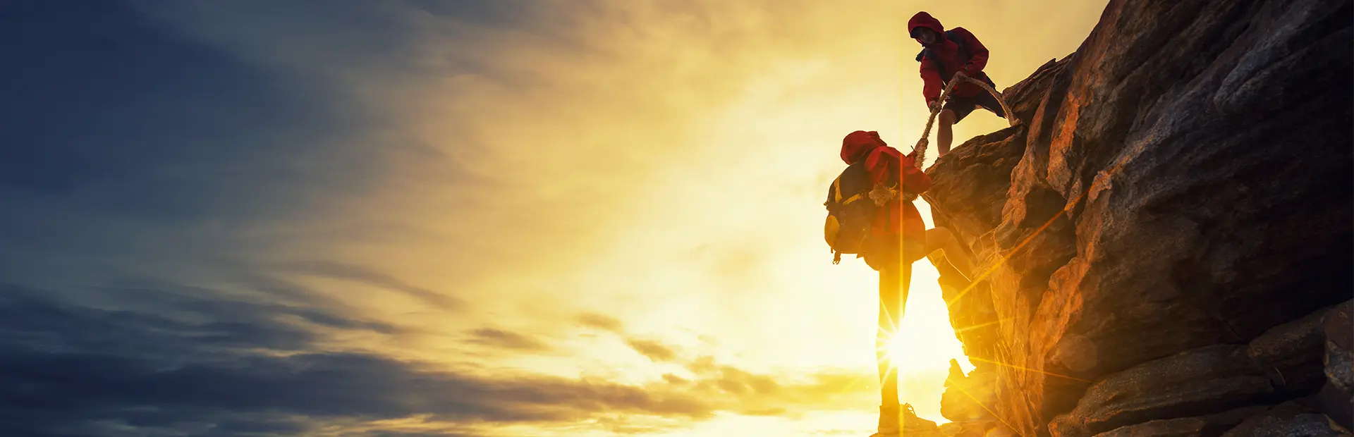 Two climbers working together to climb up a rock face.