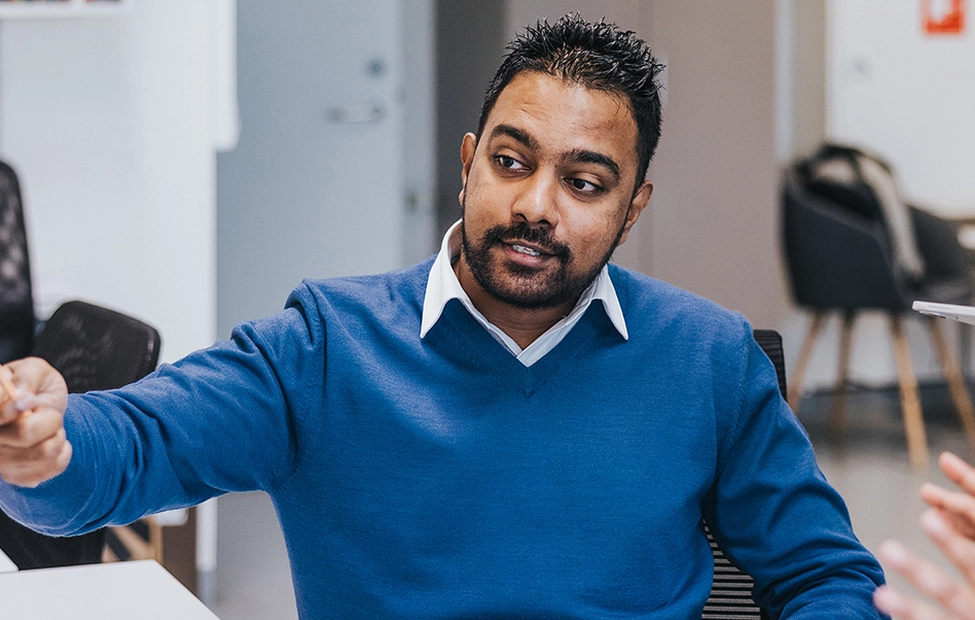 A man, seated in an office, pointing at a computer screen