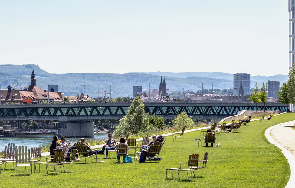 A panoramic view of Basel, from the Novartis Campus with people lounging in the foreground and the black forest in the background