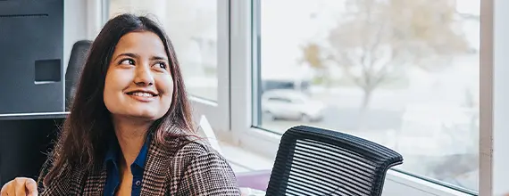 A woman, seated in an office, looking side-ways out of a window