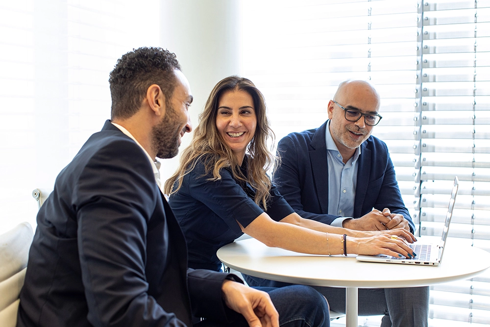 A group of three business people,a woman and two men, seated and working together in-front of a laptop