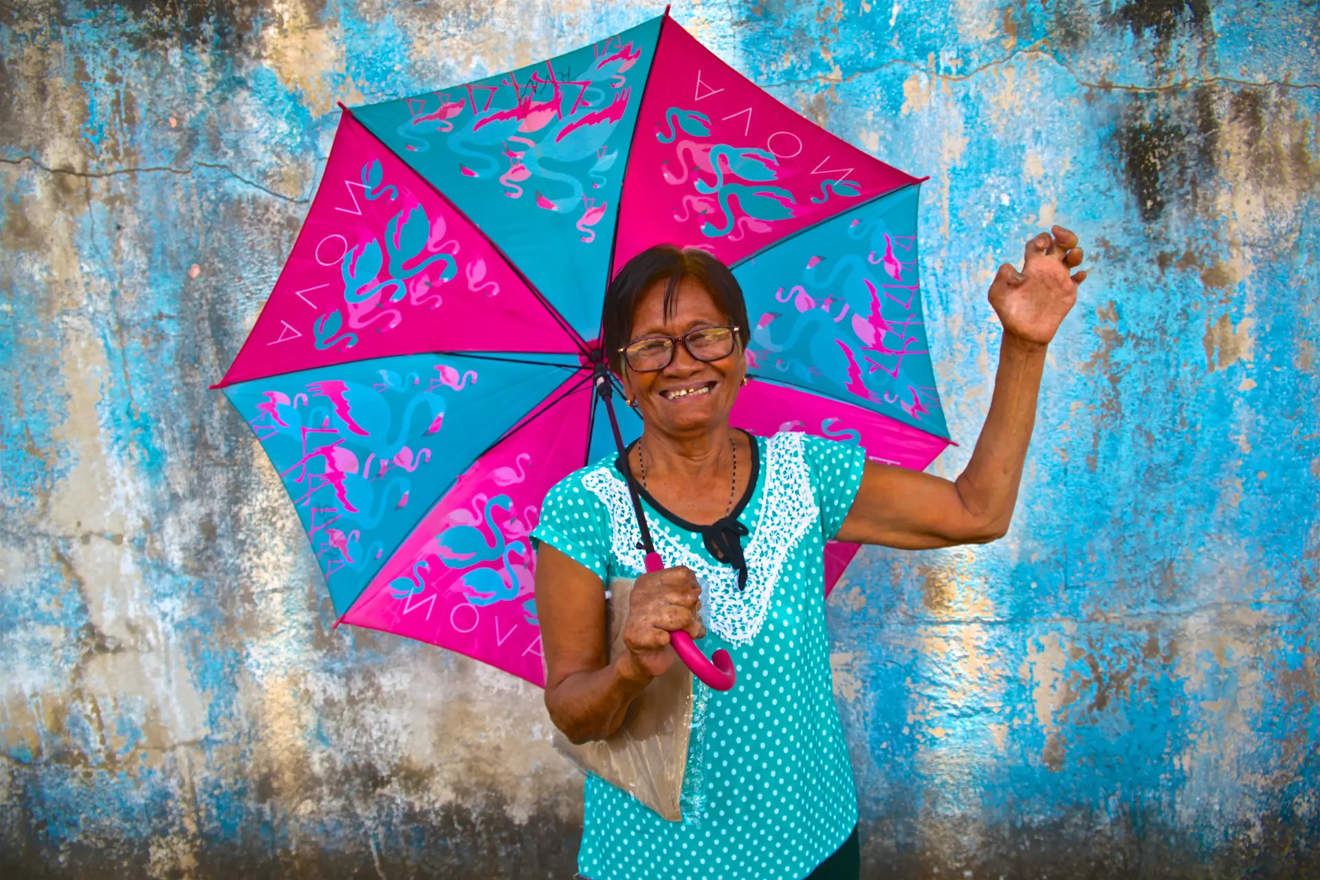 A leprosy patient with grade 2 disabilities in the Philippines holding a parasol and waving at the camera.