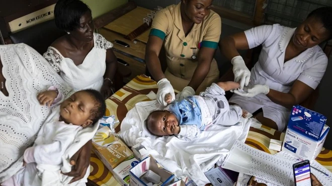 A mother holding baby in a clinic, surrounded by nurses